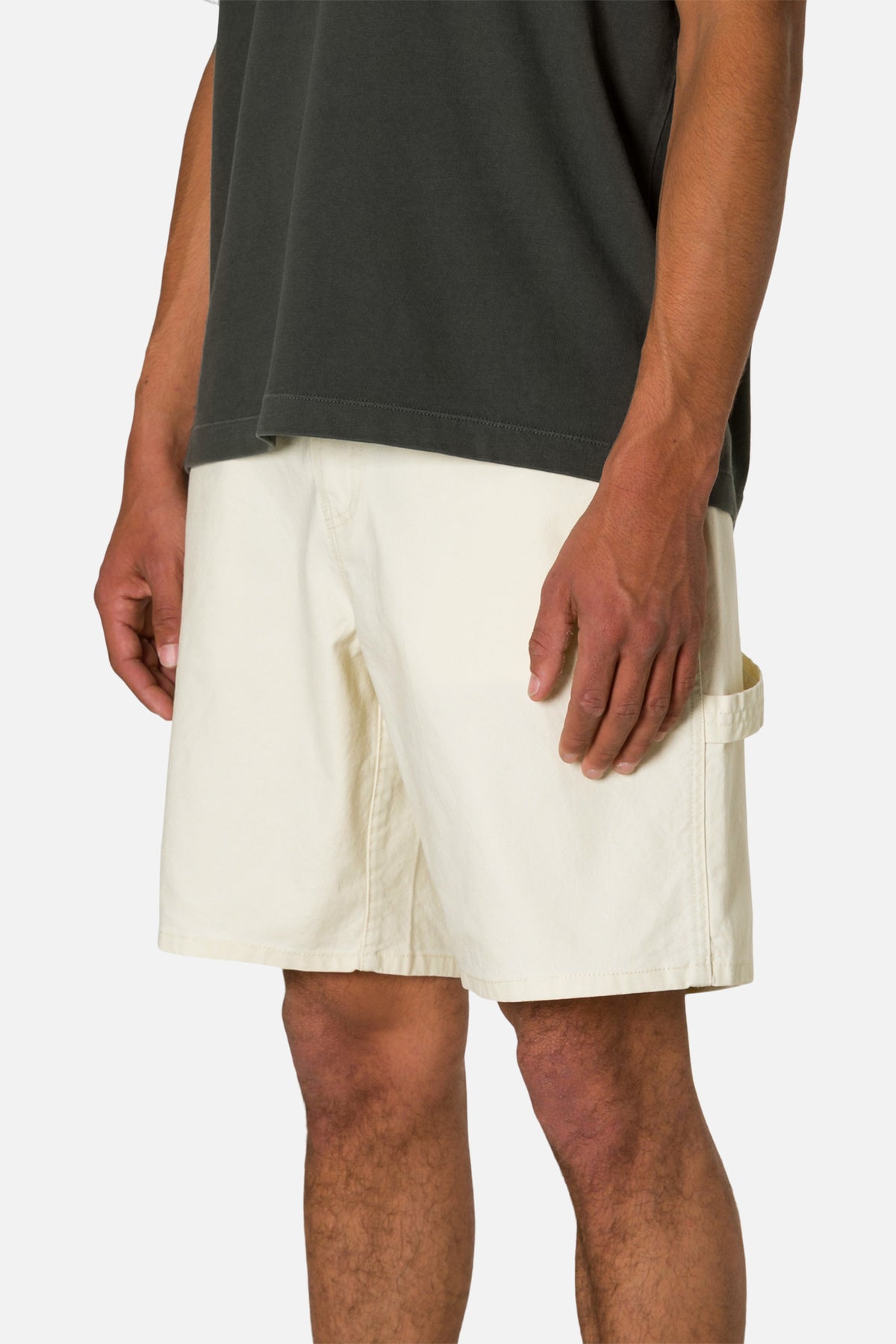 Side view person wearing off white shorts and a black shirt on a plain background