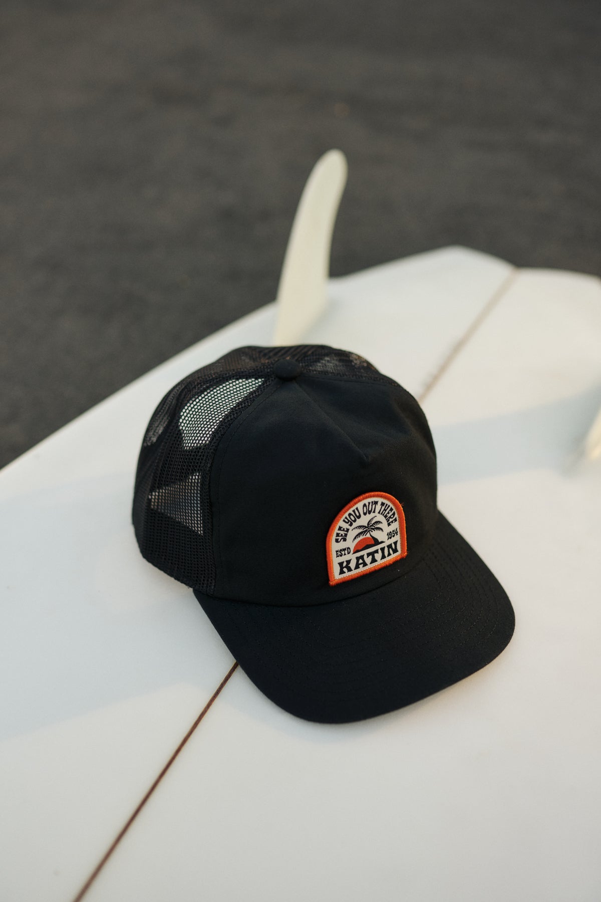 Black cap with a patch on a white surfboard against a dark background