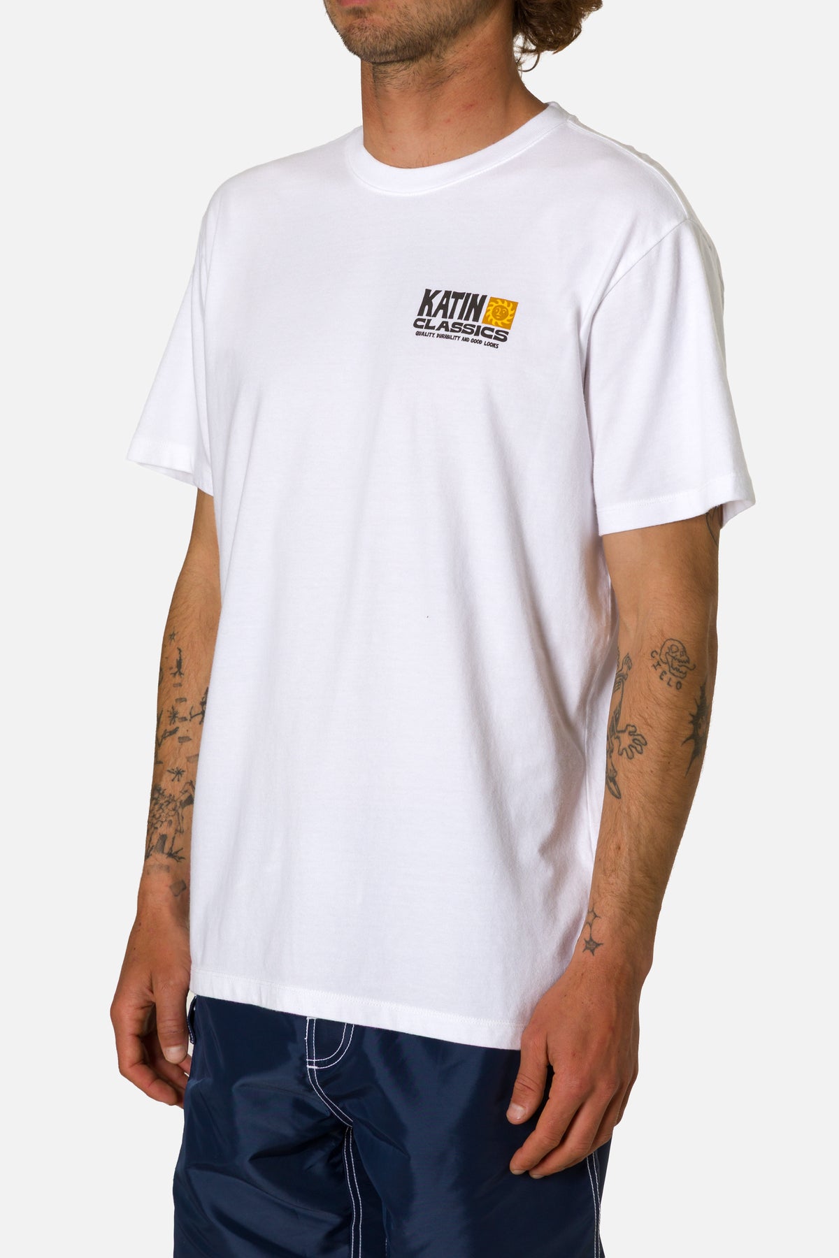 Person wearing a white t-shirt with a logo on a plain background