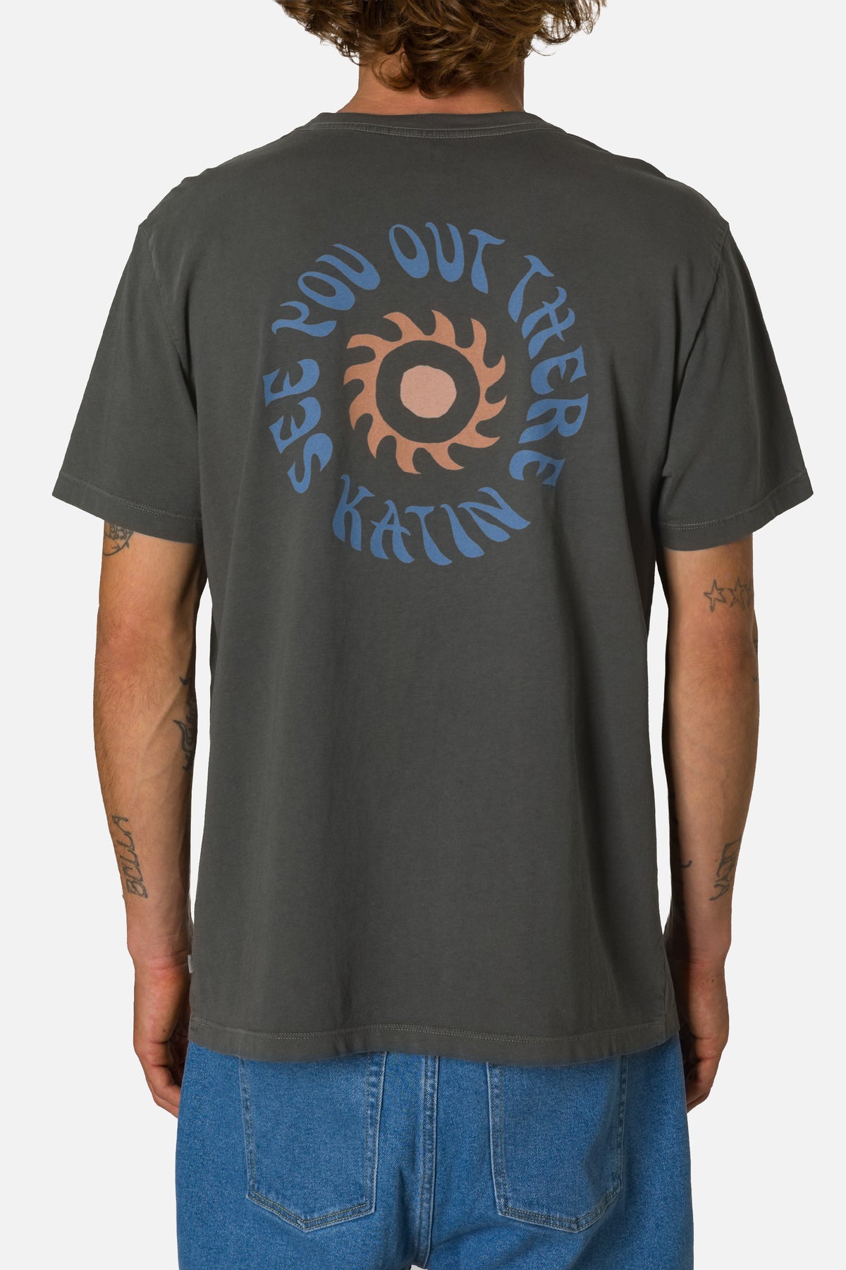 Person wearing a dark gray t-shirt with a See you out there graphic design on the back, standing against a white background.