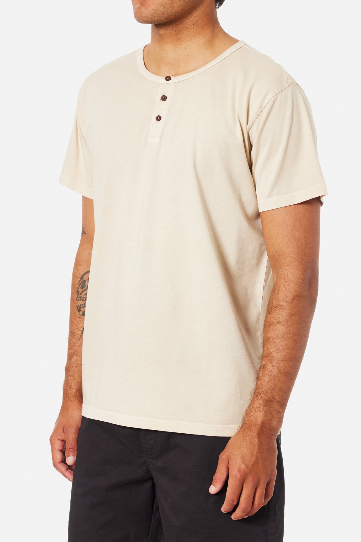 A person wearing a off white Henley shirt and blue jeans on a white background 
