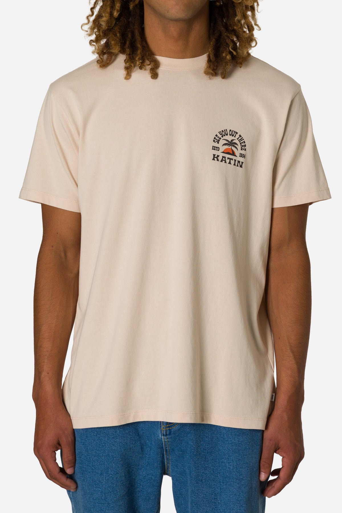 Person wearing a beige t-shirt with a logo on a plain background