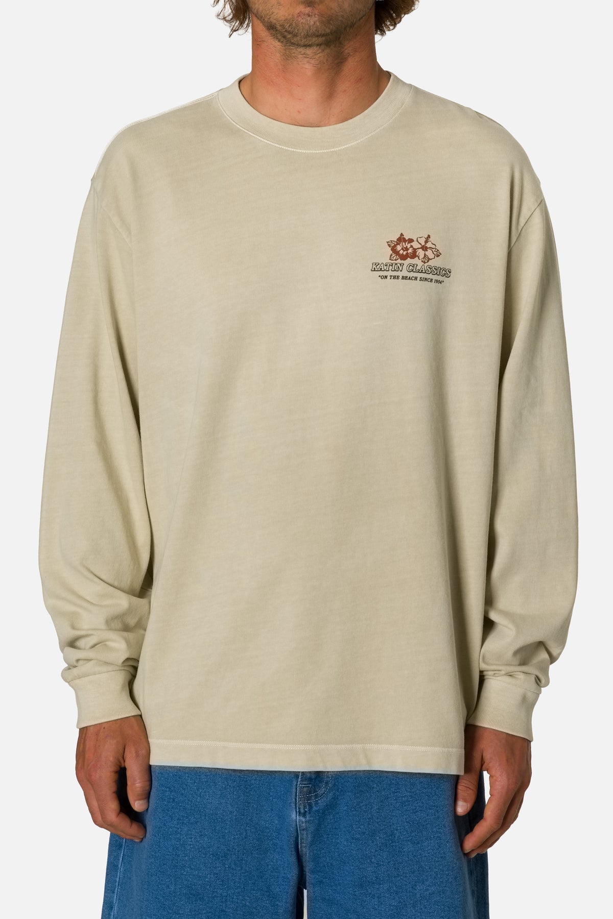 Person wearing a beige long-sleeve shirt with a logo on a white background