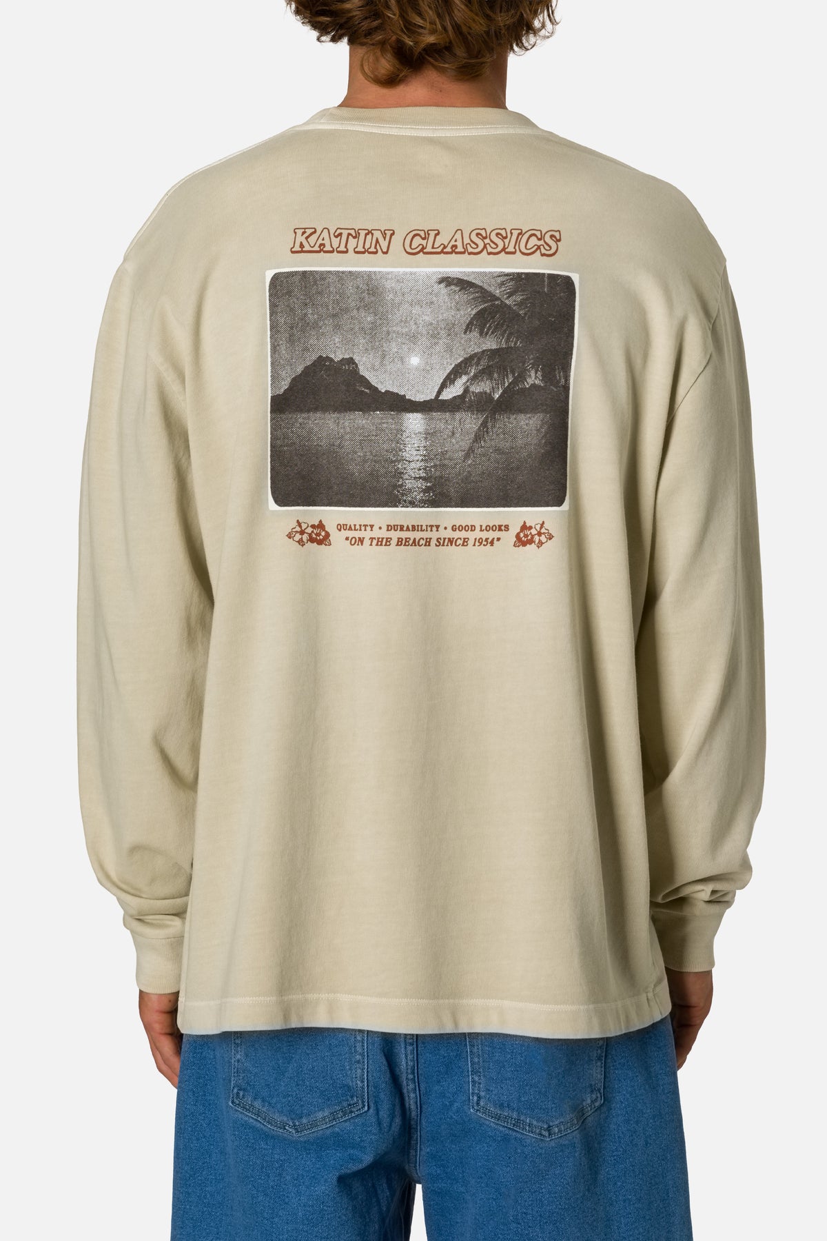 Beige long-sleeve shirt with a graphic design on the back, worn by a person.