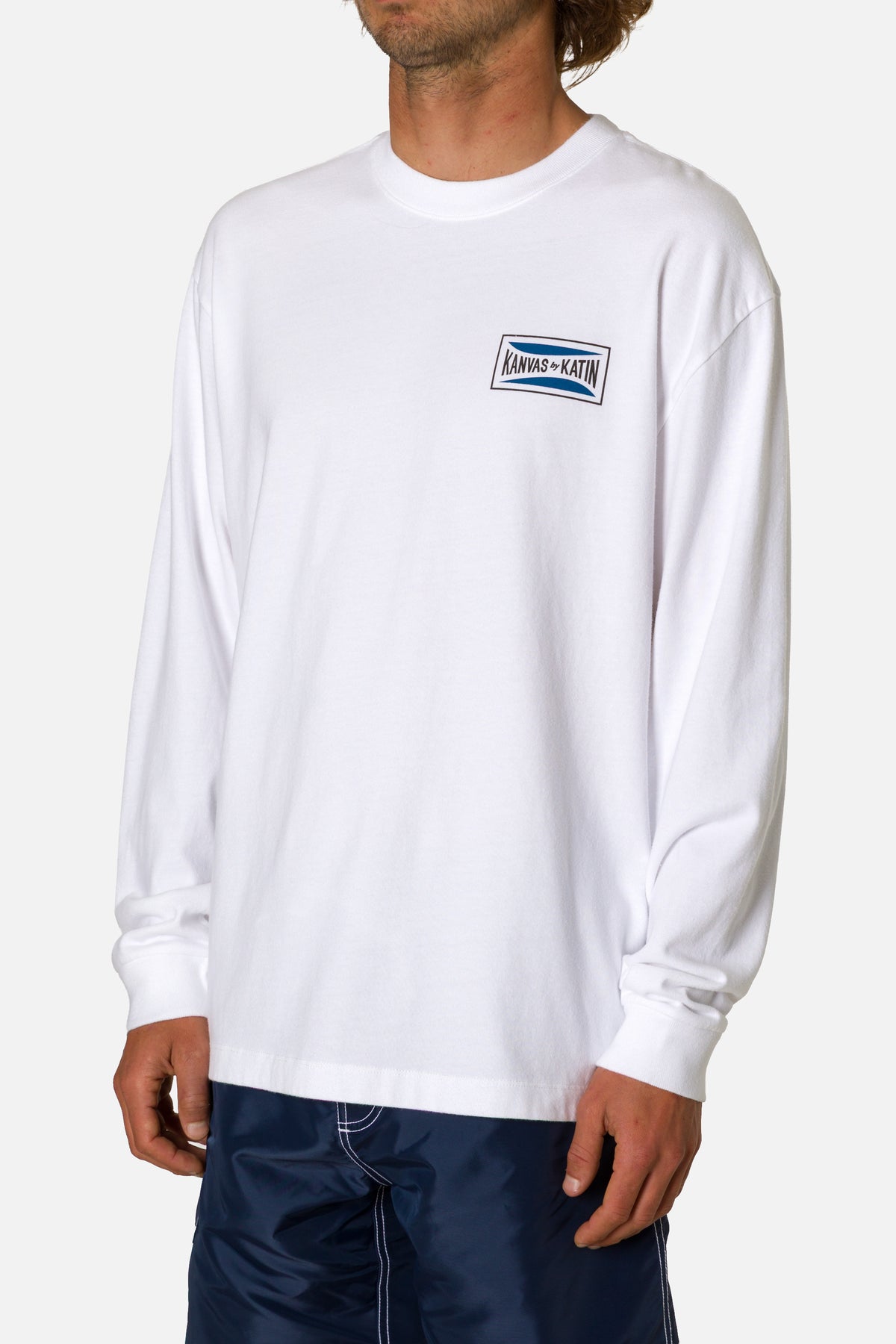 Person wearing a white long-sleeve shirt with a logo on a plain background