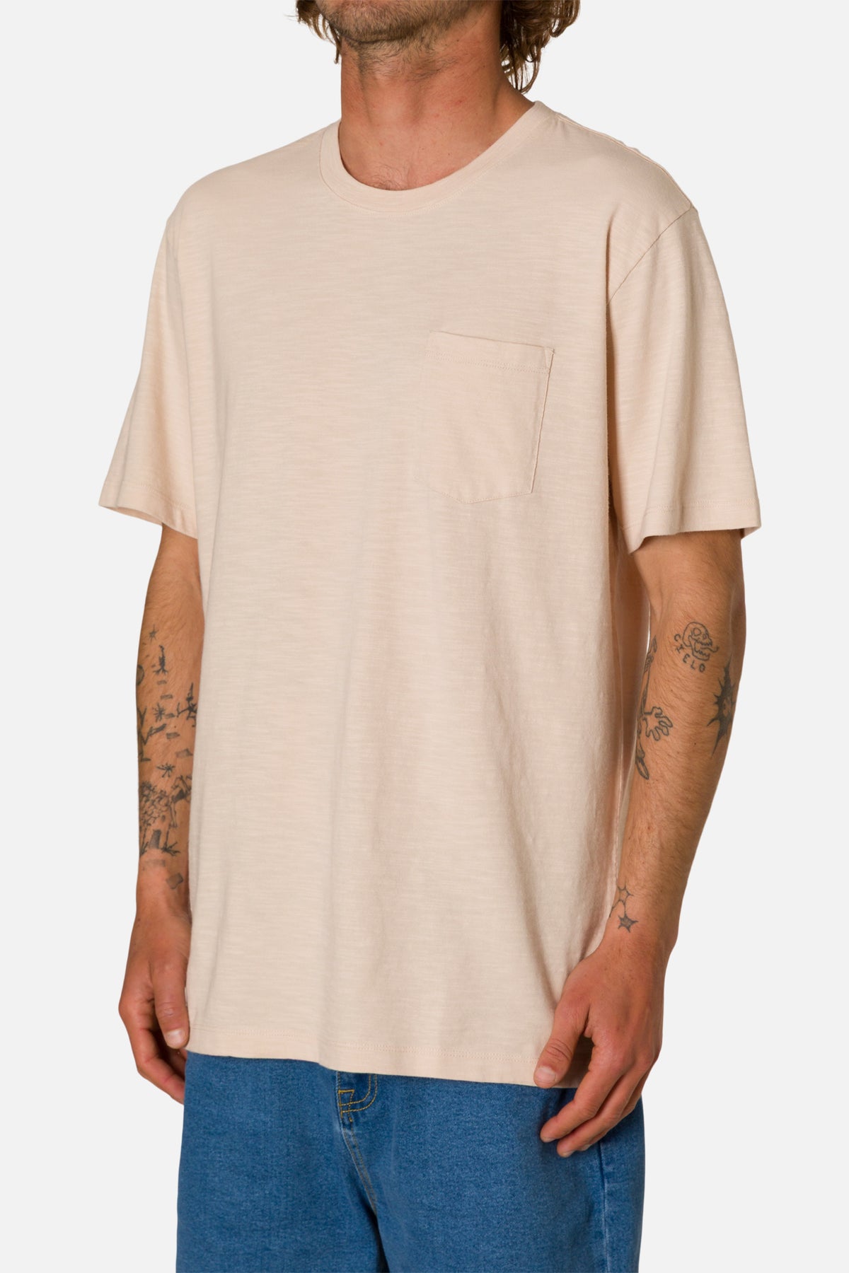 Man wearing a beige t-shirt and blue jeans on a white background
