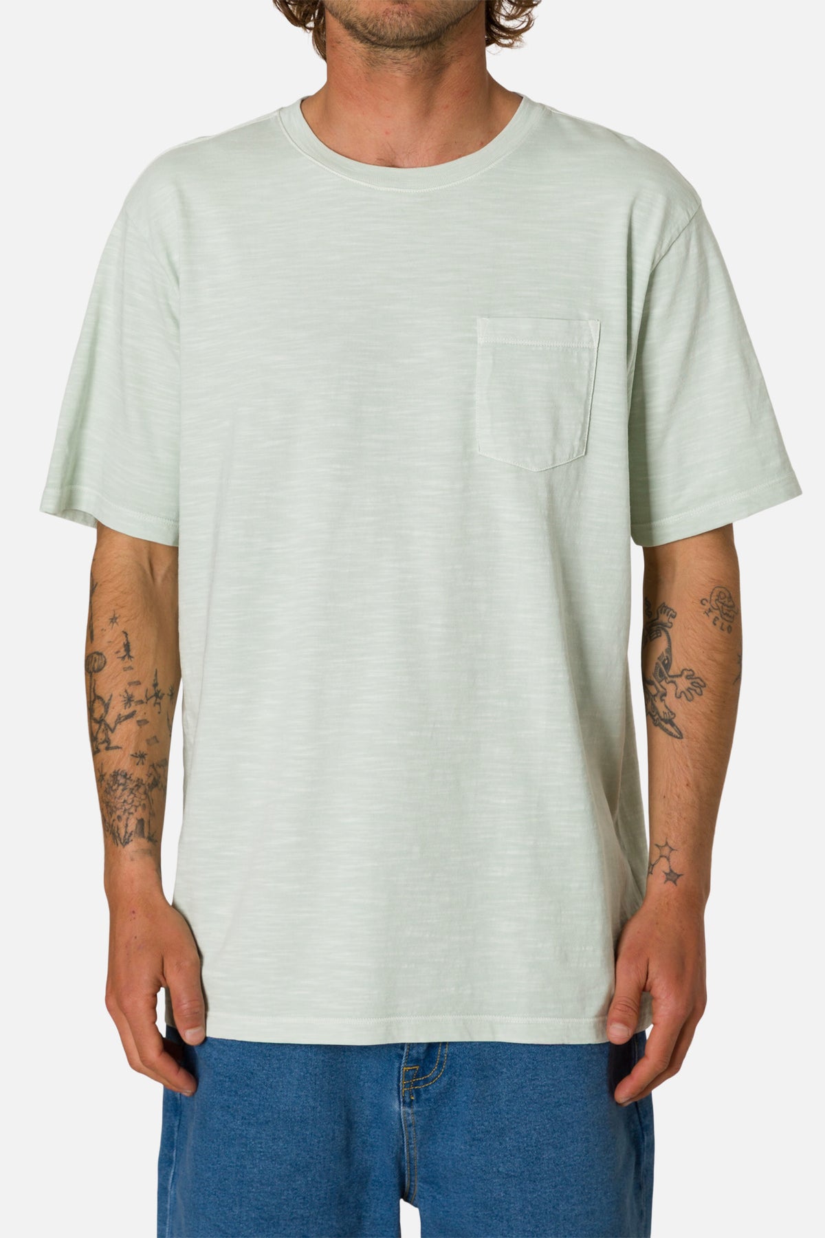 Person wearing a light green t-shirt with a pocket on a white background