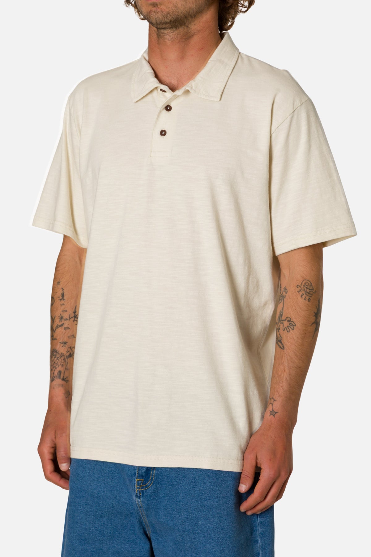 Man wearing a beige polo shirt and blue jeans on a white background