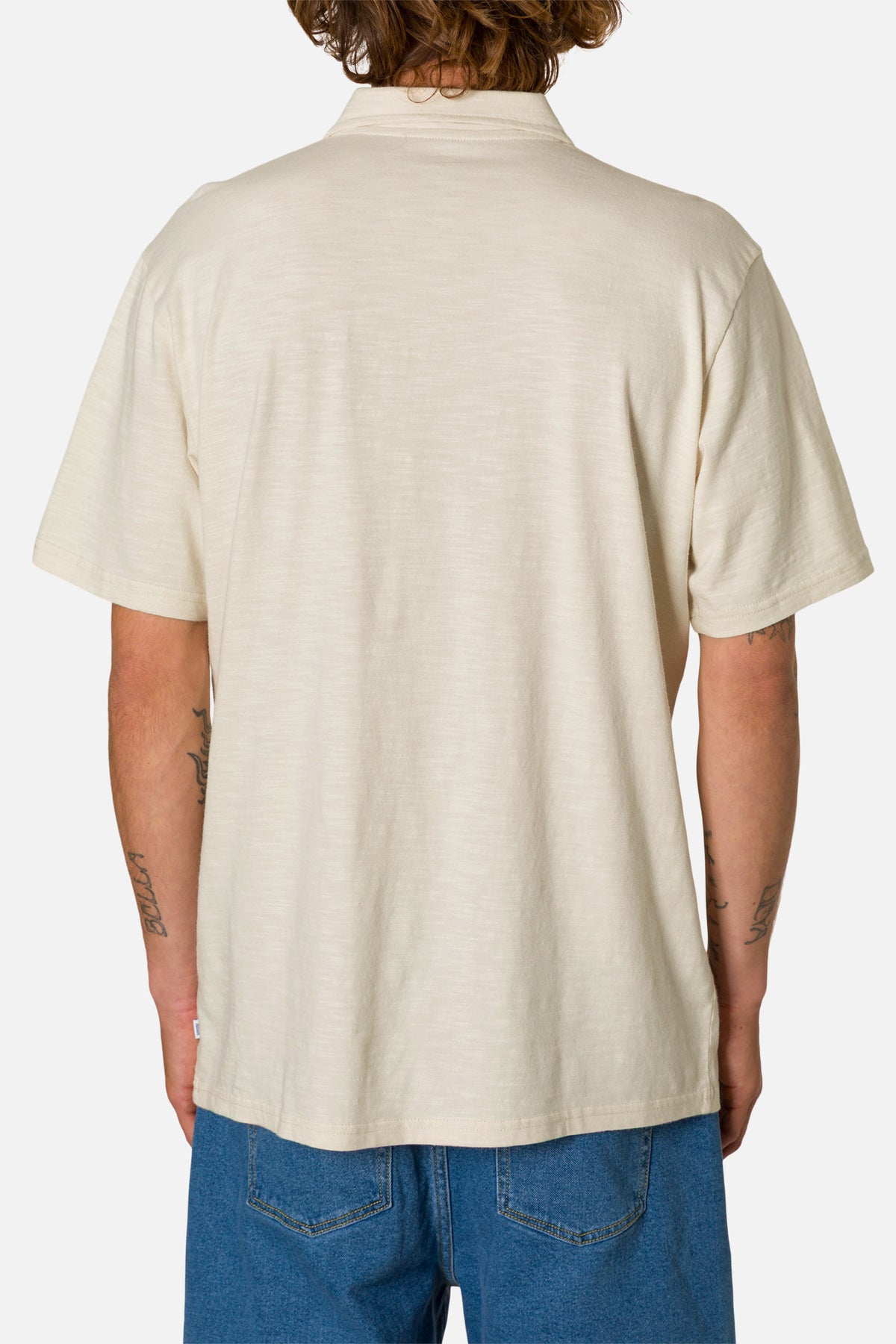 Person wearing a beige polo shirt and blue jeans on a white background