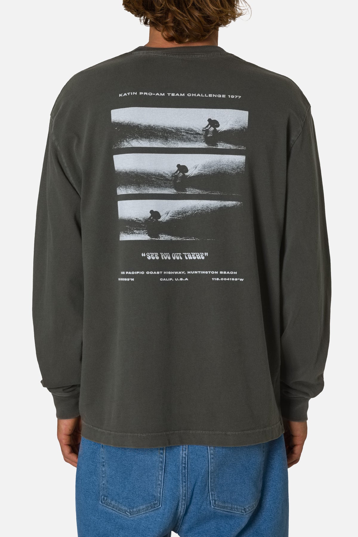 Person wearing a dark gray long-sleeve shirt with a graphic design on the back, standing against a white background.