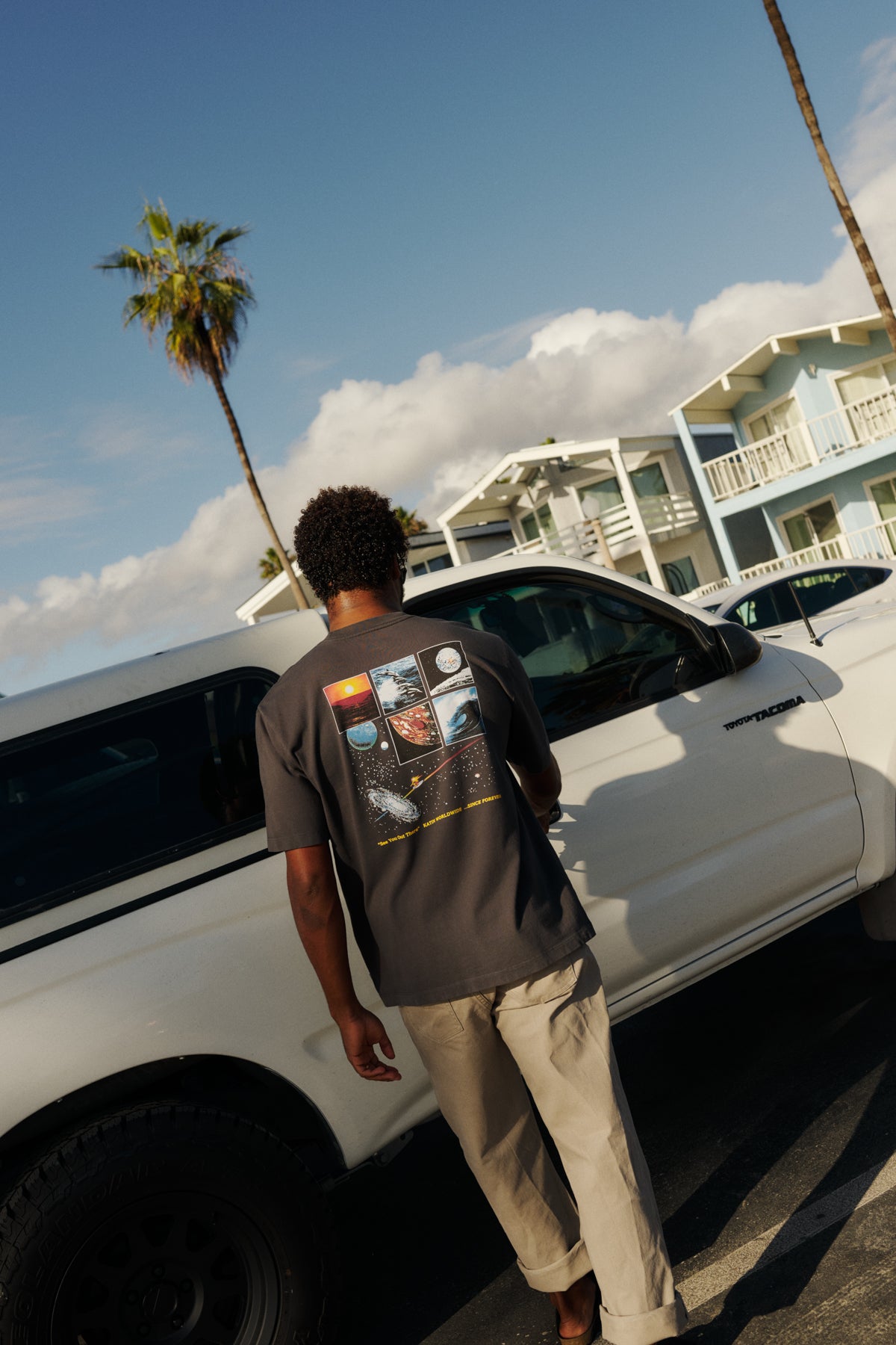 Man standing next to a white van with palm trees and a building in the background